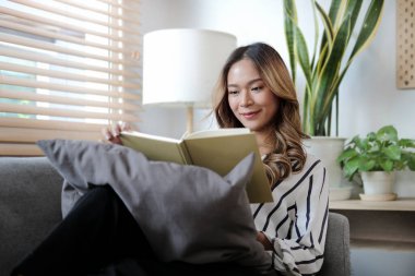 Evdeki kanepede otururken kitap okuyan güzel bir genç kadın. İnsanlar ve eğlence konsepti.