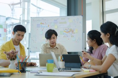 Modern ofis ortamında masanın etrafında oturan yaratıcı genç insanlar ve birlikte yeni bir proje üzerinde çalışıyorlar..