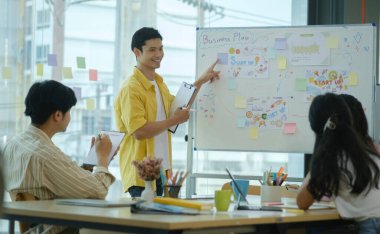 Yakışıklı Asyalı iş adamı beyaz tahtaya işaret ederken, meslektaşlarına niyetle yeni bir proje sunuyor..