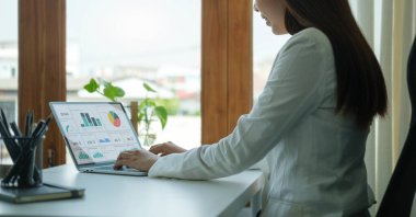 Young asian female office worker sitting in bright office and working on computer laptop.	