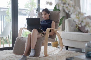 Gülümseyen genç kadın rahat koltukta oturuyor ve dijital tablet kullanıyor..