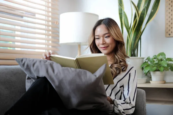 Evdeki kanepede otururken kitap okuyan güzel bir genç kadın. İnsanlar ve eğlence konsepti.