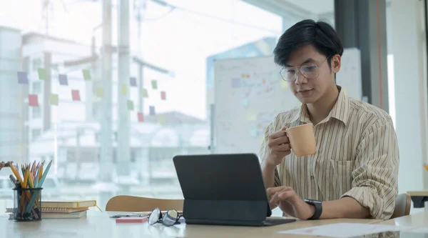 一个英俊的商人拿着咖啡杯 在有创意的办公室里使用电脑笔记本电脑 — 图库照片