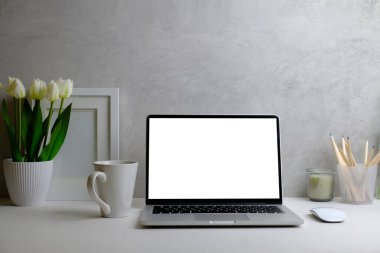 İçişleri Bakanlığı. Bilgisayar dizüstü, resim çerçevesi, kahve fincanı, defter ve çiçek saksısı beyaz masada..