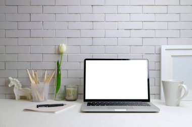 Laptop bilgisayarı, resim çerçevesi, kahve fincanı ve kalem tutacağı olan ofis masası tuğla duvara dayalı..