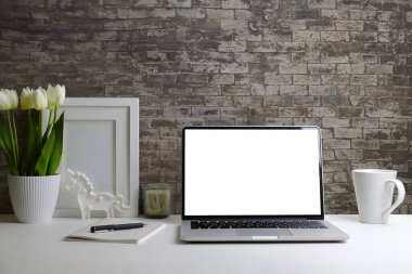 Laptop bilgisayarı, ev bitkisi ve resim çerçevesi olan modern bir iş yeri. Metin reklamı için boş ekran.