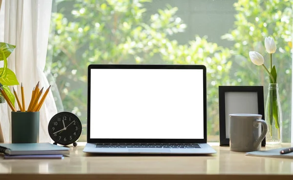 Boş ekranlı dizüstü bilgisayar, kahve fincanı, kalem tutacağı ve parlak oturma odasındaki ahşap masada resim çerçevesi..