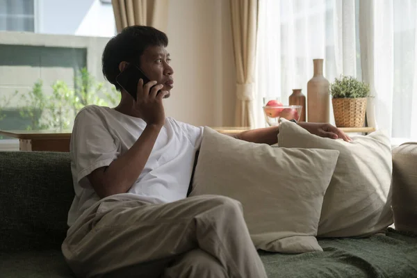 Thoughtful Asian Male Talking Mobile Phone While Resting Couch Home — Zdjęcie stockowe