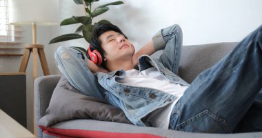 Happy young asian man closing her eyes and listening to music with wireless headphone.	