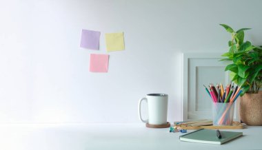 Işık duvarında saksı bitkisi, kırtasiye malzemesi, hesap makinesi ve renkli yapışkan notları olan yaratıcı iş yeri.