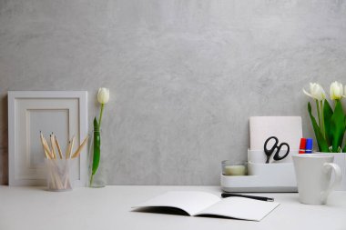 Home office interior. Picture frame, coffee cup, notebook and pencil holder on white table against. Copy space.	