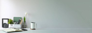 Home office interior. Houseplant, coffee cup, books and pencil holder on white table.	