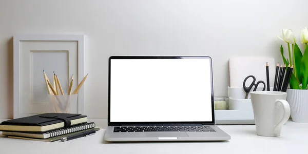 Computer laptop with blank screen, flower pot, coffee cup and picture frame on white table.	