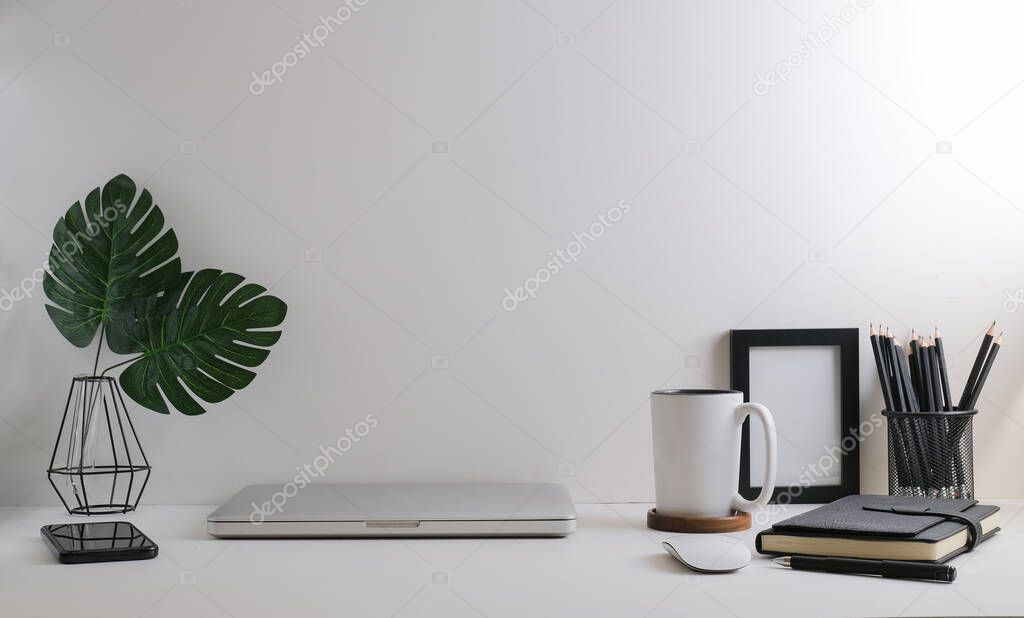 Comfortable workplace with laptop, stationery, picture frame and potted plant on white table.	