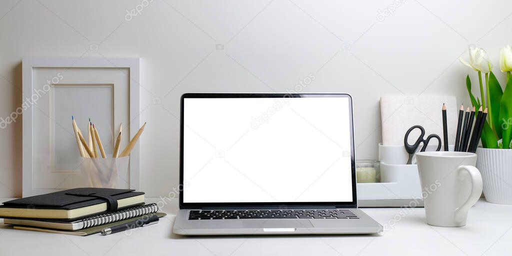 Computer laptop with blank screen, flower pot, coffee cup and picture frame on white table.	