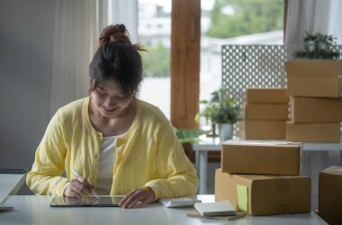 Karton kutuların yanında oturan küçük işletme sahibi başlat ve dijital tablet üzerinde çevrimiçi alışverişi kontrol et.