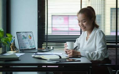 Relaxed businesswoman looking at laptop computer and drinking coffee.	