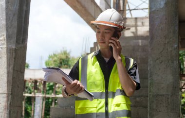 İnşaat mühendisinin inşaat sahasında dikilirken telefonla konuşması..