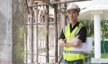 İnşaat alanında kolları bağlı duran kasklı, kendine güvenen inşaat mühendisi..