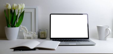 Workplace comfortable with computer laptop, coffee cup, notebook, picture frame and flower pot.	
