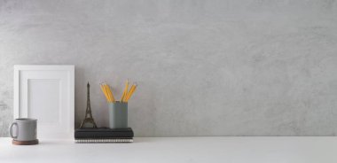 Boş çerçeveli, kalem tutacağı, beyaz masadaki beyaz duvarlı kitap ve kahve fincanı olan şık bir iş yeri. Metnin için boşluk kopyala.