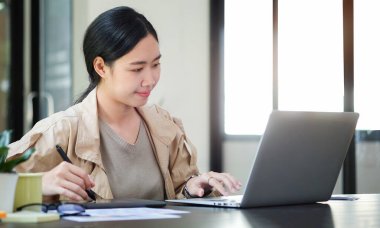 Young asian woman sitting in creative office and working with laptop computer.	