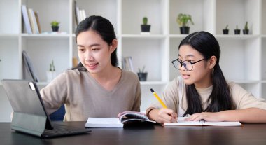 Gülümseyen Asyalı anne, küçük tatlı kızına ev ödevi yaparken yardım ediyor..