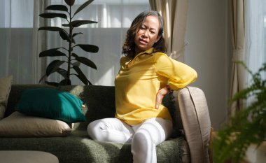 Mutsuz, olgun bir kadın dokunuyor, sırtına masaj yapıyor, sırt ağrısı çekiyor. Sağlık, acı, stres, yaş ve insan kavramı.