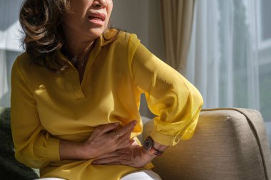 Mutsuz yaşlı bir kadın ellerini karnına koyuyor, karın ağrısı çekiyor, güçlü mide ağrısı, mide iltihabı belirtileri gösteriyor..