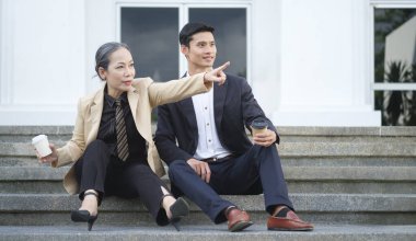 Ofisin dışındaki merdivenlerde oturmuş birbiriyle konuşan iki iş adamı..