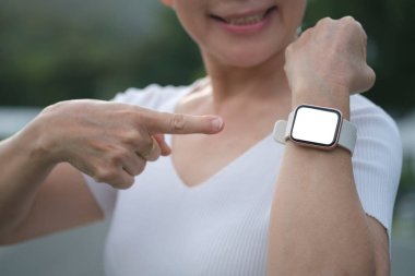 Gülümseyen orta yaşlı kadın akıllı saat sergisini işaret ediyor, sabah antrenmanından sonra yakılan kalorilerle gurur duyuyor. Fitness, sağlıklı yaşam tarzı konsepti. 