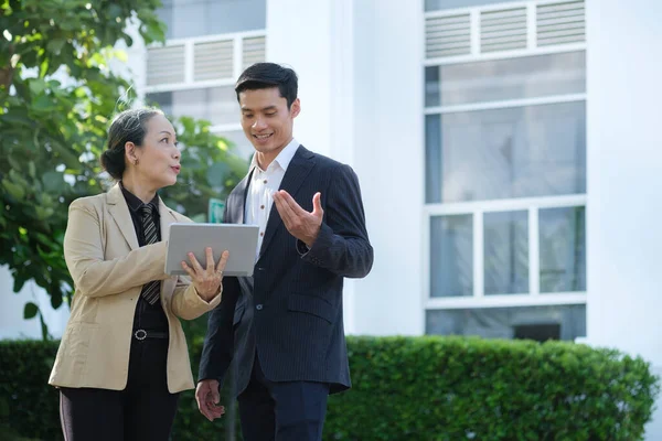 Shot of two successful business people talking to each other while standing in front of the office building.