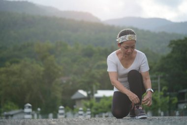 Bağcıklarını bağlayan orta yaşlı, sportif bir kadın, sabahleyin egzersiz yapmaya hazırlan. Spor, egzersiz ve doğa sporu..