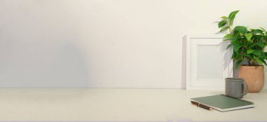 Beyaz masa üzerinde resim çerçevesi, kahve, kırtasiye ve ev bitkisi olan rahat bir iş yeri.