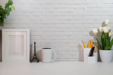 Stylish workplace with coffee cup, stationery and houseplant on white table against brick wall. Home office desk.	