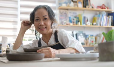 Olgun kadın küçük işletme sahibi el yapımı el işi mağazasında oturuyor ve kameraya gülümsüyor..