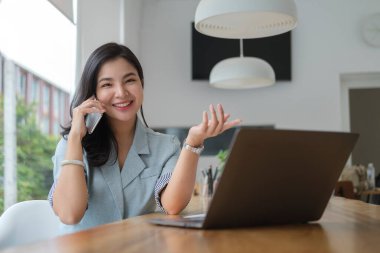 İş kadını ofiste otururken cep telefonuyla konuşuyor.