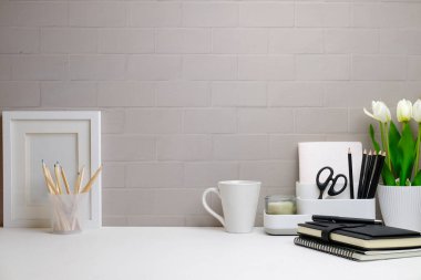 Önden boş resim çerçevesi, ev bitkisi, kalem tutacağı, beyaz masadaki kitap ve kahve fincanı. En küçük işyeri, metin için alanı kopyala.