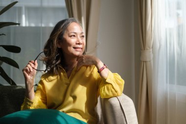 Orta yaşlı bir kadın rahat koltukta dinleniyor, başka yere bakıyor, hayal kuruyor stresten uzak, huzurlu bir ruh halinin keyfini çıkarıyor oturma odasında yalnızken..