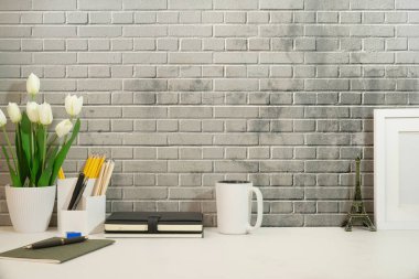 Önden boş resim çerçevesi, ev bitkisi, kalem tutacağı, beyaz masadaki kitap ve kahve fincanı. En küçük işyeri, metin için alanı kopyala.