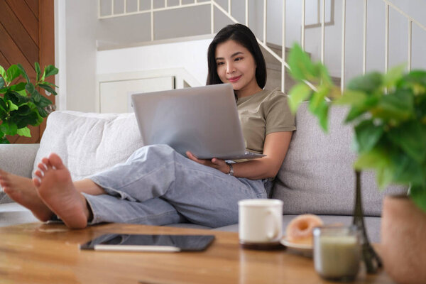 Smiling asian woman sitting on couch using laptop computer.	
