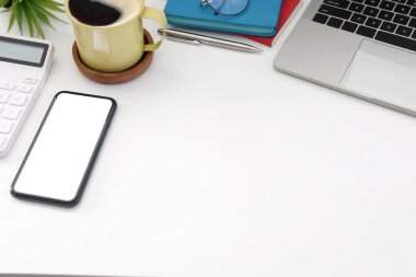 Mockup smart phone, calculator, coffee cup and wireless earphone on white office desk.	