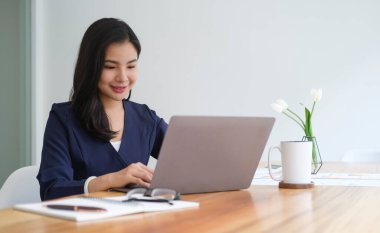 Young asian female office worker sitting in bright office and working on computer laptop.	