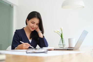 Attractive young businesswoman sitting in modern office and using digital tablet.