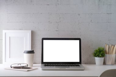 Home office desk with laptop computer, picture frame, coffee cup, and pencil holder on white table against brick wall.	