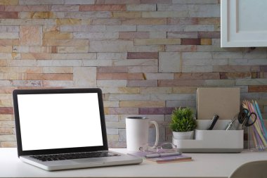 Ev bilgisayarı, resim çerçevesi, ev bitkisi ve kırtasiye malzemeleri beyaz masada. Modern işyeri.