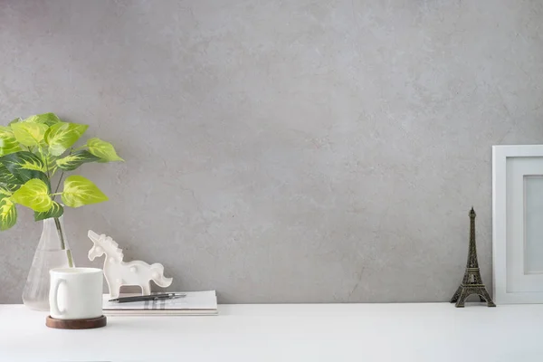 Comfortable workplace with picture frame, coffee, stationery and houseplant on white table.	