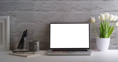 Dizüstü bilgisayarı, kahve fincanını, kırtasiyeyi, resim çerçevesini ve saksıyı beyaz masaya koyun. Reklam metniniz için boş ekran.