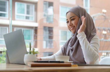 Başörtüsü takan Müslüman iş kadını dizüstü bilgisayar kullanıyor, ekiple görüntülü konuşma yapıyor..