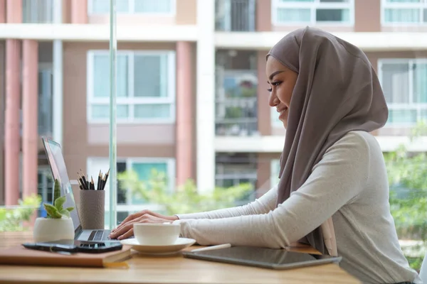 Side view young businesswoman wearing hijab working with laptop in modern workplace.